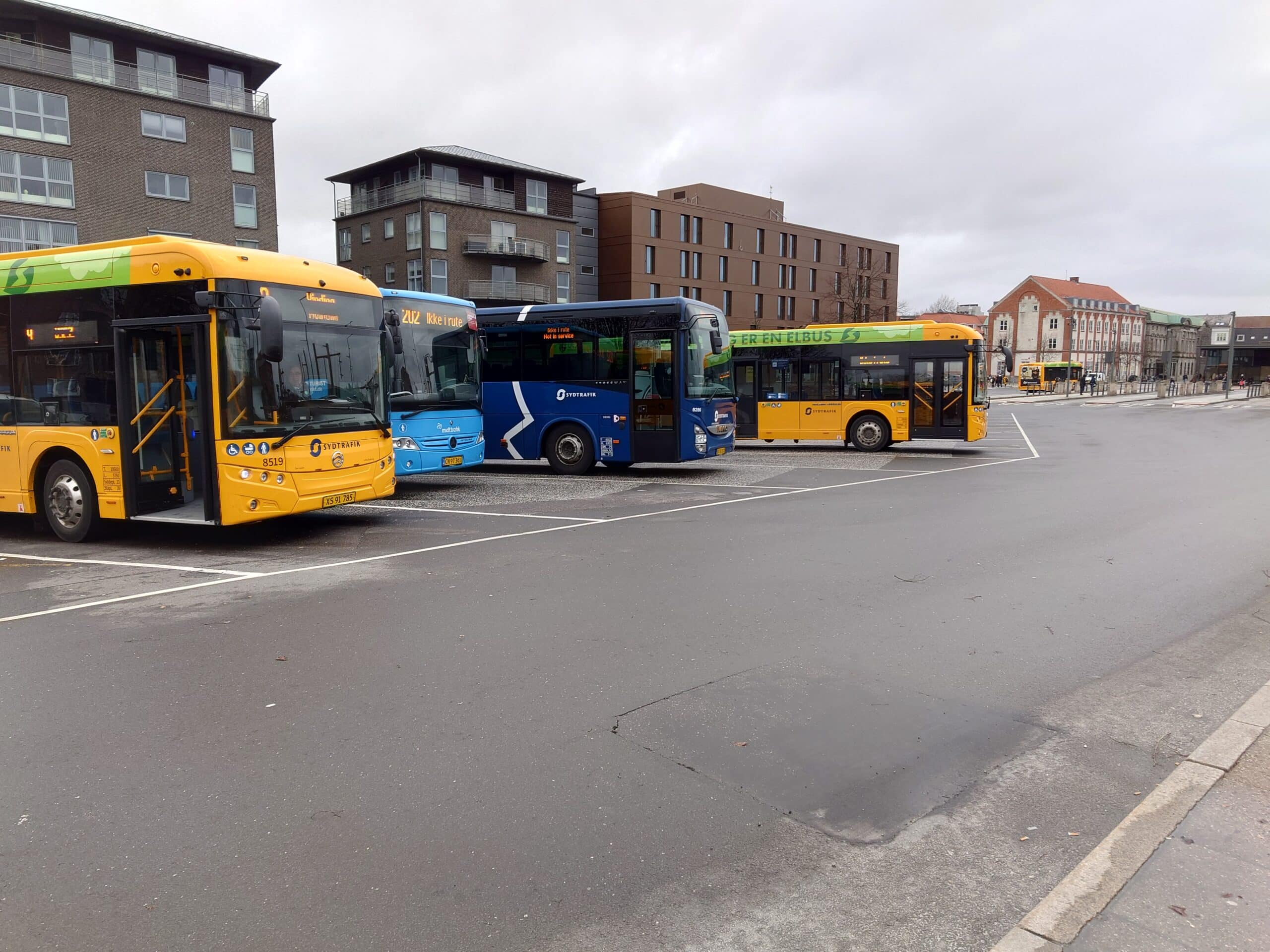 to gule busser og en blå bus der holder parkeret på en busstation
